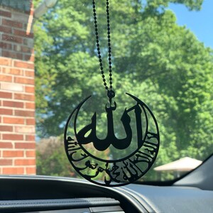 قلادة سوداء معلقة على مرآة السيارة تحمل اسم الله والشهادة