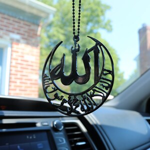 قلادة سوداء معلقة على مرآة السيارة تحمل اسم الله والشهادة