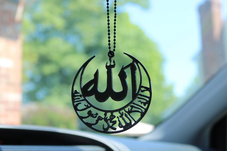 قلادة سوداء معلقة على مرآة السيارة تحمل اسم الله والشهادة