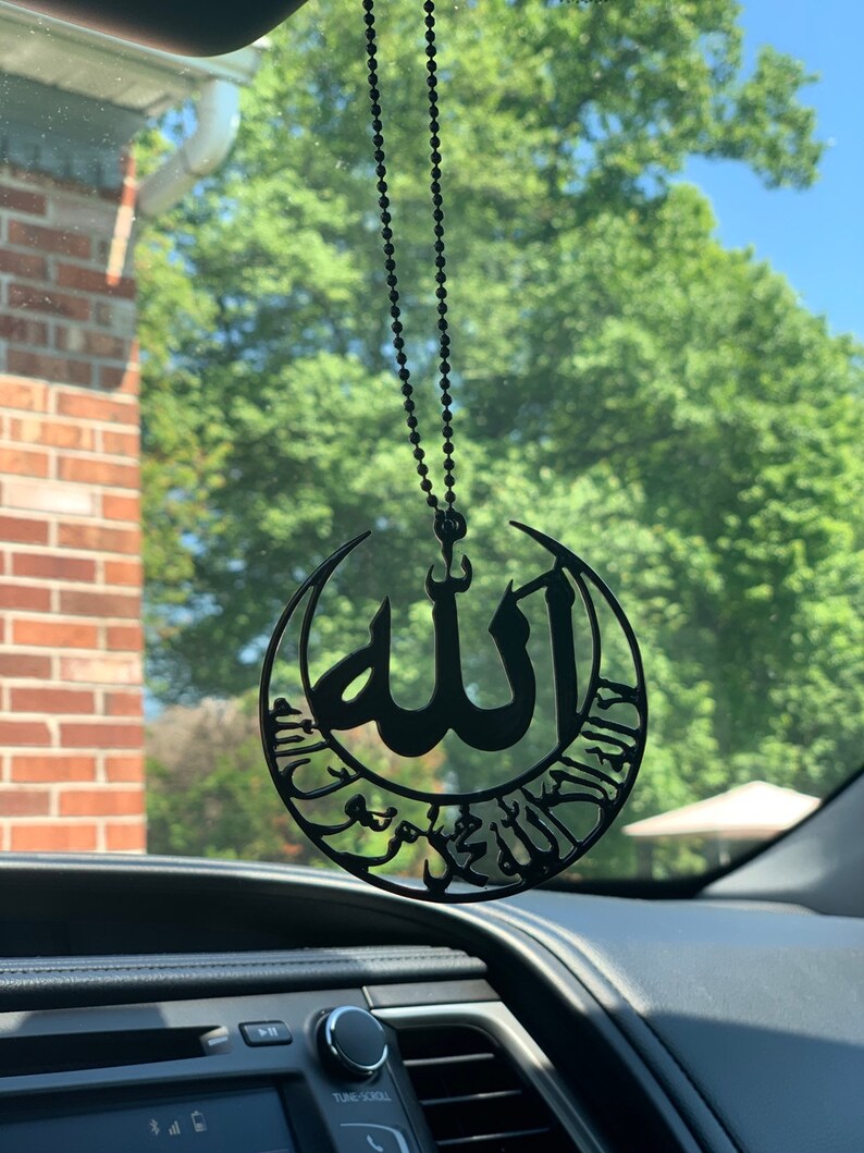 قلادة سوداء معلقة على مرآة السيارة تحمل اسم الله والشهادة